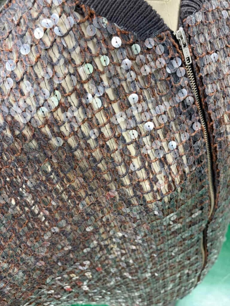 Close-up detail of appliqué and cording embroidery on a sequin garment.